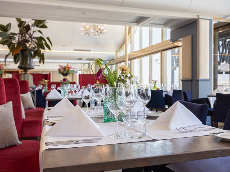 Restaurant Waves met glazen wanden en uitzicht op de pier. De tafels zijn gedekt met servetten, glazen en kaarsen